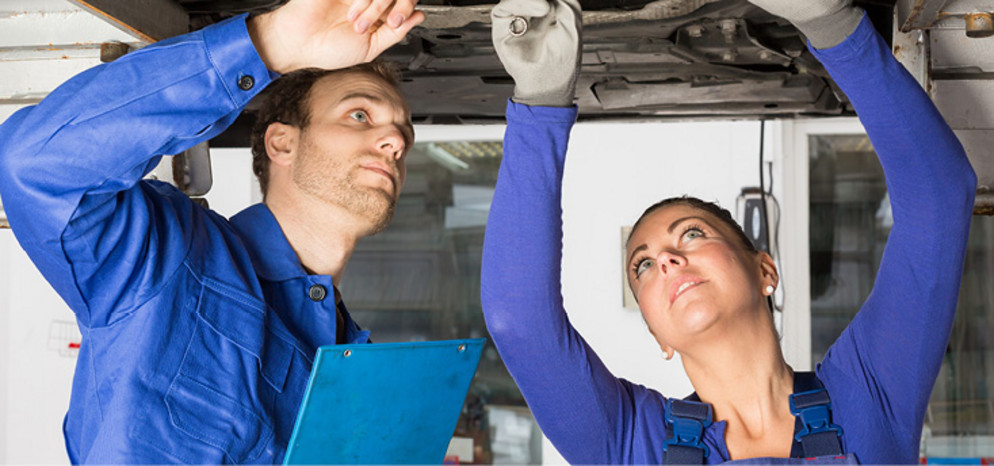 Zwei Mechatroniker arbeiten an einem Auto, was auf einer Bühne steht